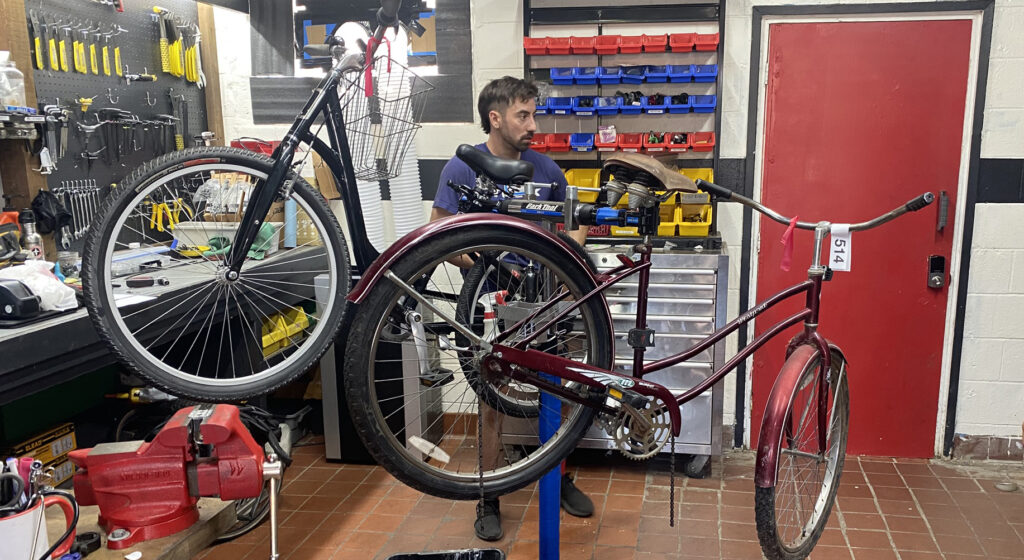 A man stands working on a bike mounted on a stand. 
