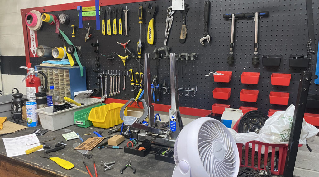 IMG_2654-crop Various bike repair tools hang on a wall and are on a work bench.