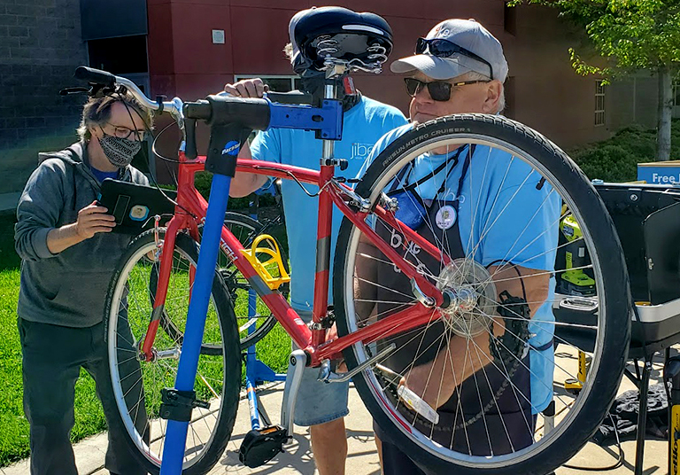Two men work on a bike while another man looks at a tablet.